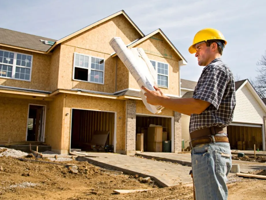 Pekerja konstruksi memeriksa cetak biru di depan rumah yang sedang dibangun